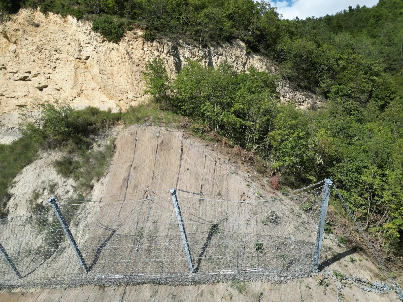 Dettaglio di barriera paramassi: montanti in acciaio, funi e rete sotto la parete