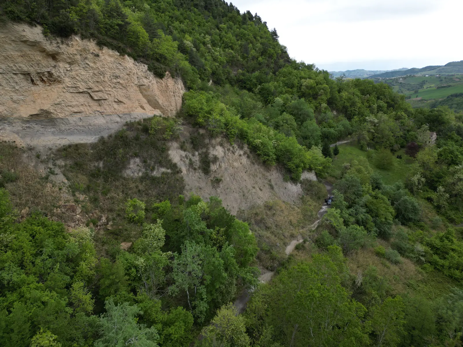 Vista da drone del versante prima dei lavori: ciglio roccioso, scarpata erosa e vegetazione
