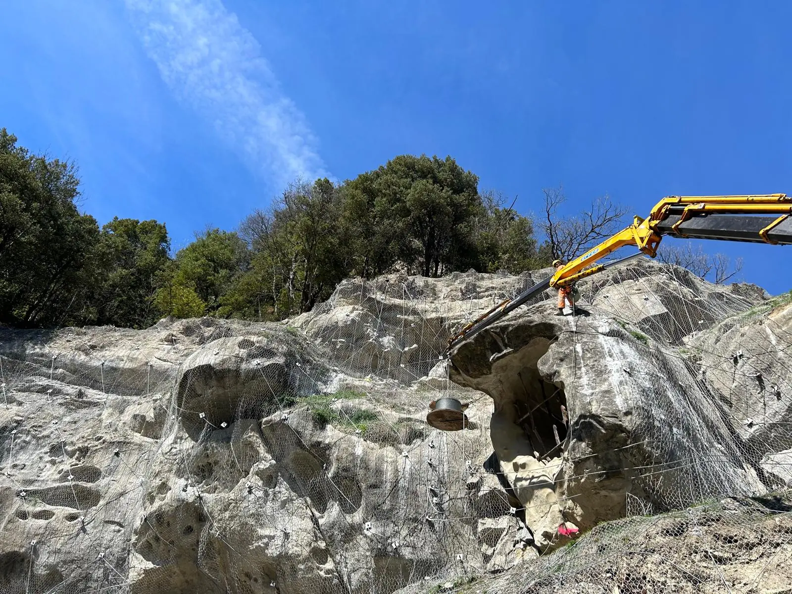 Parete rocciosa rivestita con rete metallica, operatore sul cestello di un’autogru