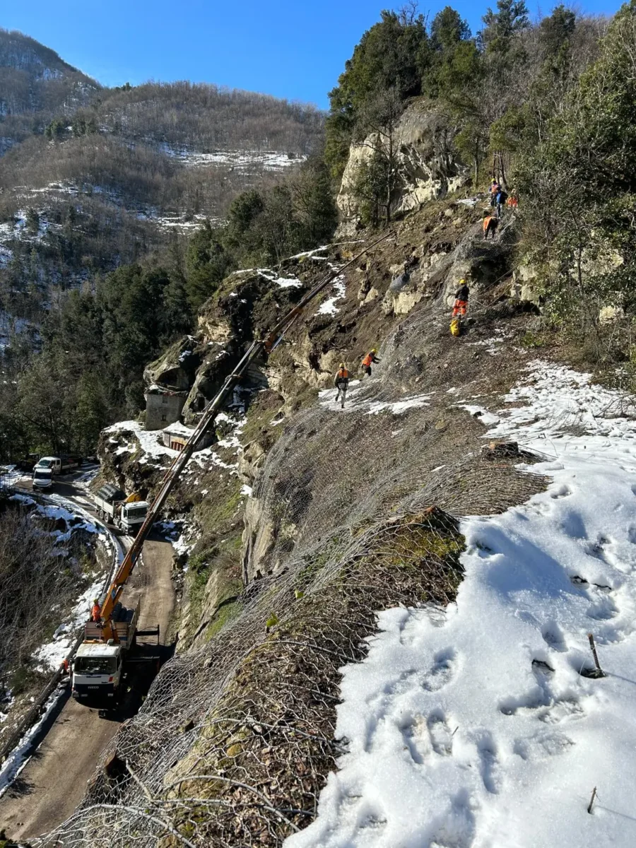 Rocciatori in parete su un versante innevato, con autogru sulla strada sottostante
